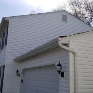 Photo showing a house and garage with white vinyl siding that has been recently restored and fully cleaned with power washing