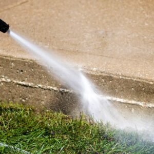 Closeup photo of pressure washer water cleaning the side of a concrete sidewalk