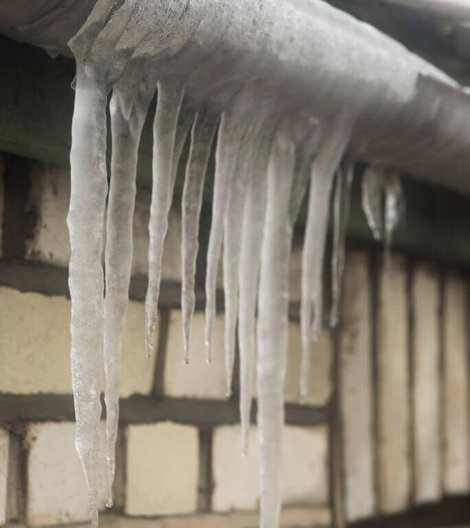 Photo of icicles hanging from a overflowing and dripping gutter