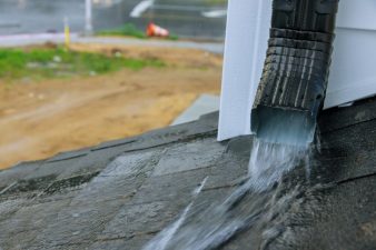 Closeup photo of a downspout with water pouring out onto a roof